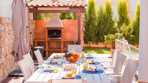 An outdoor dining area with a brick oven, white chairs, and a table set for breakfast. - Villa w/ private pool & BBQ in Varandas do Lago (Almancil)