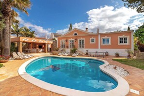 Una piscina con sillas de descanso, un patio y una casa con techo de tejas.