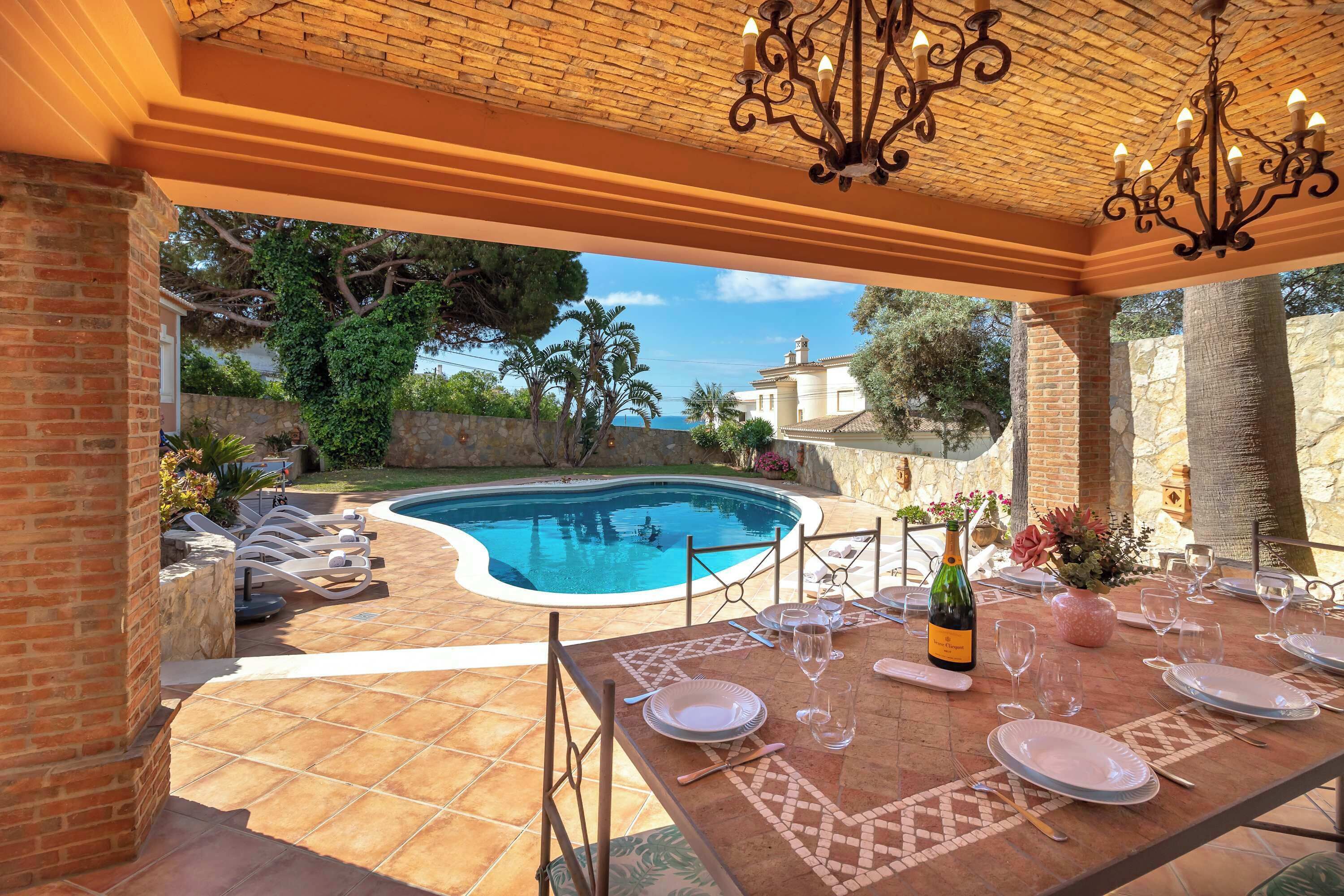 A poolside area with a table set for dining, a pool, and a view of the sea.