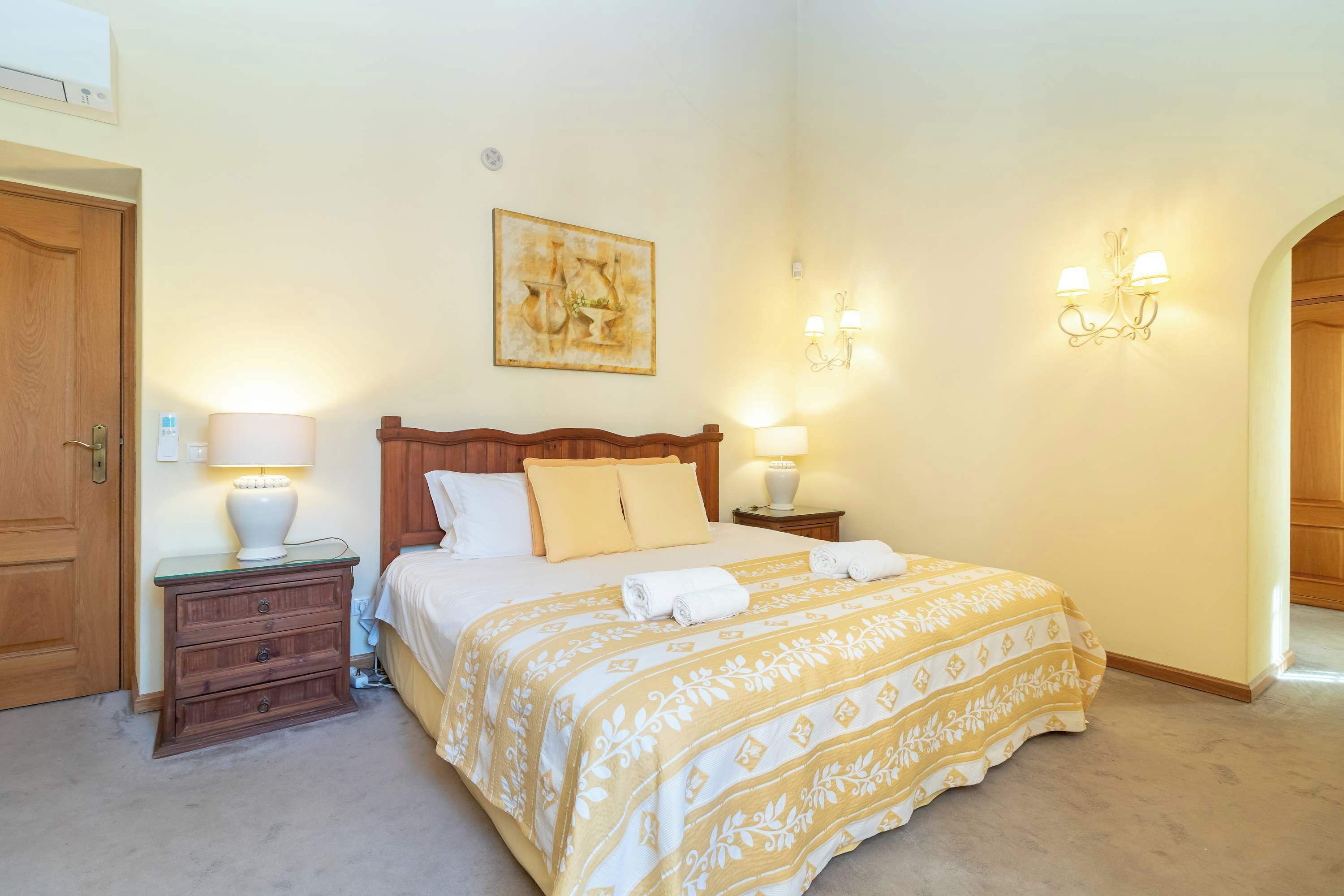 Un dormitorio con cama, mesitas de noche, lámparas, un cuadro y una araña.