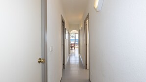 A narrow hallway with white walls and a tiled floor, leading to a room with a view of the beach. - GOLF SANT JORDI 2 Apartment (Cambrils)