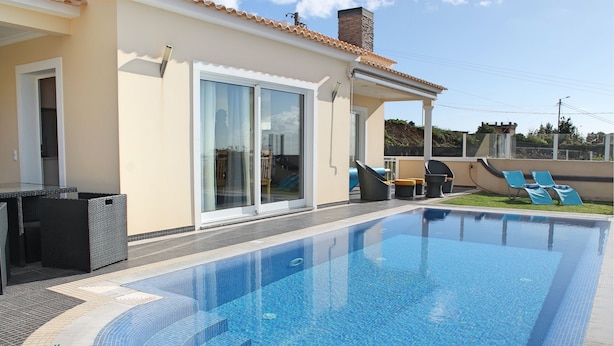 Ein Pool mit einer gefliesten Terrasse, einer überdachten Veranda und einer Glastür zu einem überdachten Außenbereich.