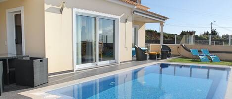 A swimming pool with a tiled deck, a covered patio area, and a sliding glass door leading to a covered outdoor space.
