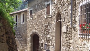 A stone building with an arched entrance, a staircase, and a window with a metal grille. - stone cottage, Medieval Village. 15 km Sea. Terrace (Castelvecchio di Rocca Barbena)