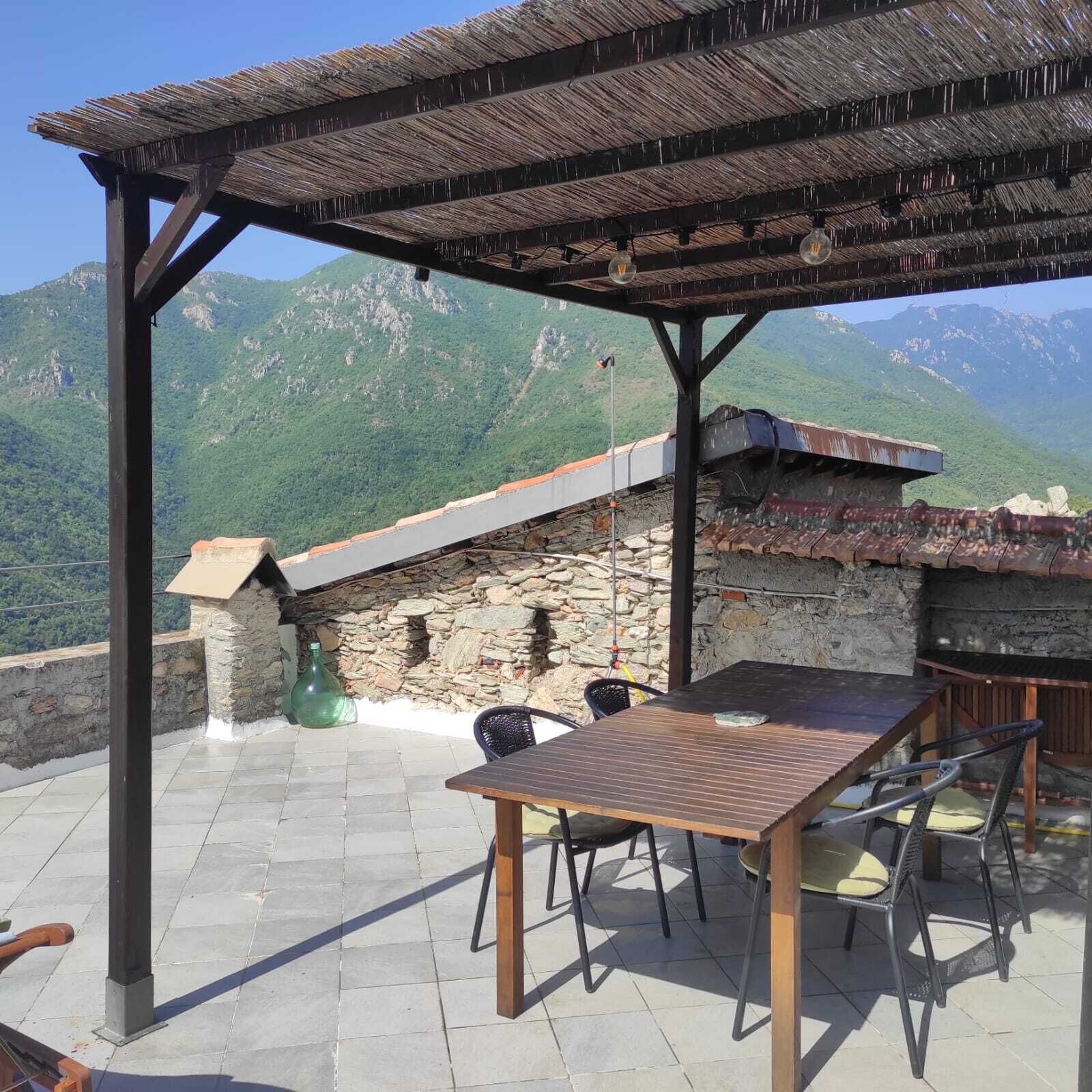 An outdoor patio with a table and chairs, a stone wall, and a view of mountains.