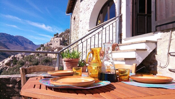A wooden table set with plates, a pitcher, and glasses on a balcony overlooking a mountainous landscape. - stone cottage, Medieval Village. 15 km Sea. Terrace (Castelvecchio di Rocca Barbena)