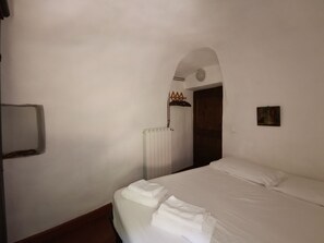 Une chambre d’hôtel avec un lit, un radiateur, une porte et un petit tableau accroché au mur.