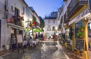 A narrow street with outdoor seating, shops, and a sign for 'Los Ques'.