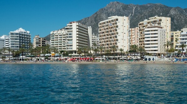 A coastal cityscape with high-rise buildings, a beach, and mountains in the background.