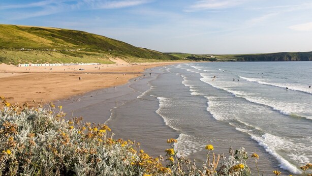 A beach with waves, a sandy shore, and green hills in the background. - 2-bedroom dog friendly cottage located in Braunton, within easy reach of the beach. (Braunton)