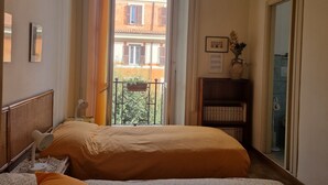 A bedroom with a large window, a bed, a bedside table with a lamp, a bookshelf, and an air conditioning unit. - Domus Costanza - Bright and elegant apartment in Piazza Verbano. (Roma)