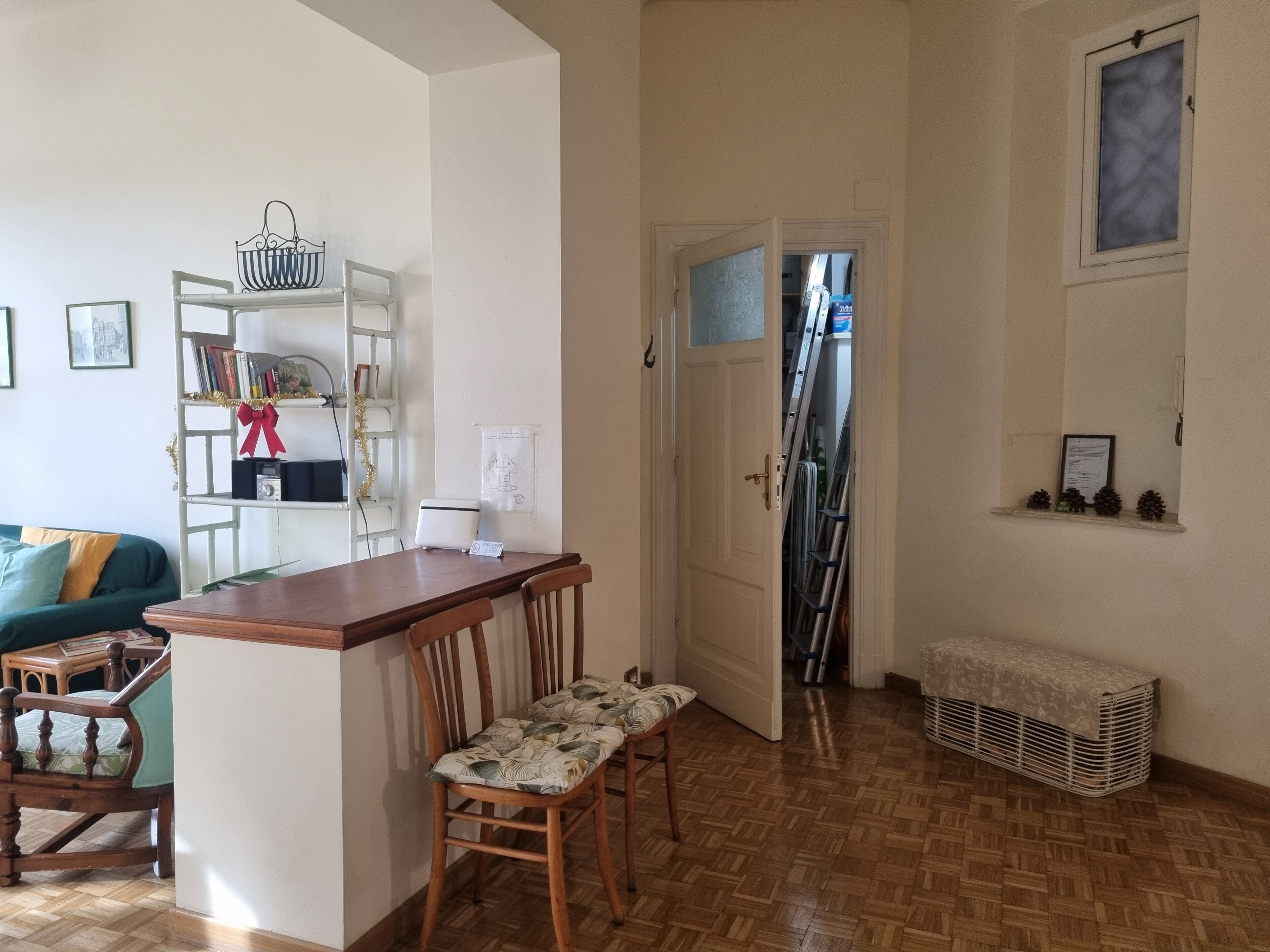 Una sala de estar acogedora con una mesa de centro de madera, un sofá y una estantería. Hay una puerta que da a otra habitación con una escalera y una ventana.