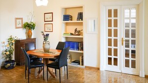 A dining area with a wooden table, black chairs, a vase with flowers, a bookshelf with books and decorative items, and a white door with glass panels. - Domus Costanza - Bright and elegant apartment in Piazza Verbano. (Roma)