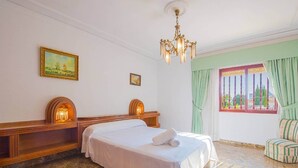 Et hotelværelse med en stor seng, en lysekrone, et vindue med gardiner og et maleri på væggen.