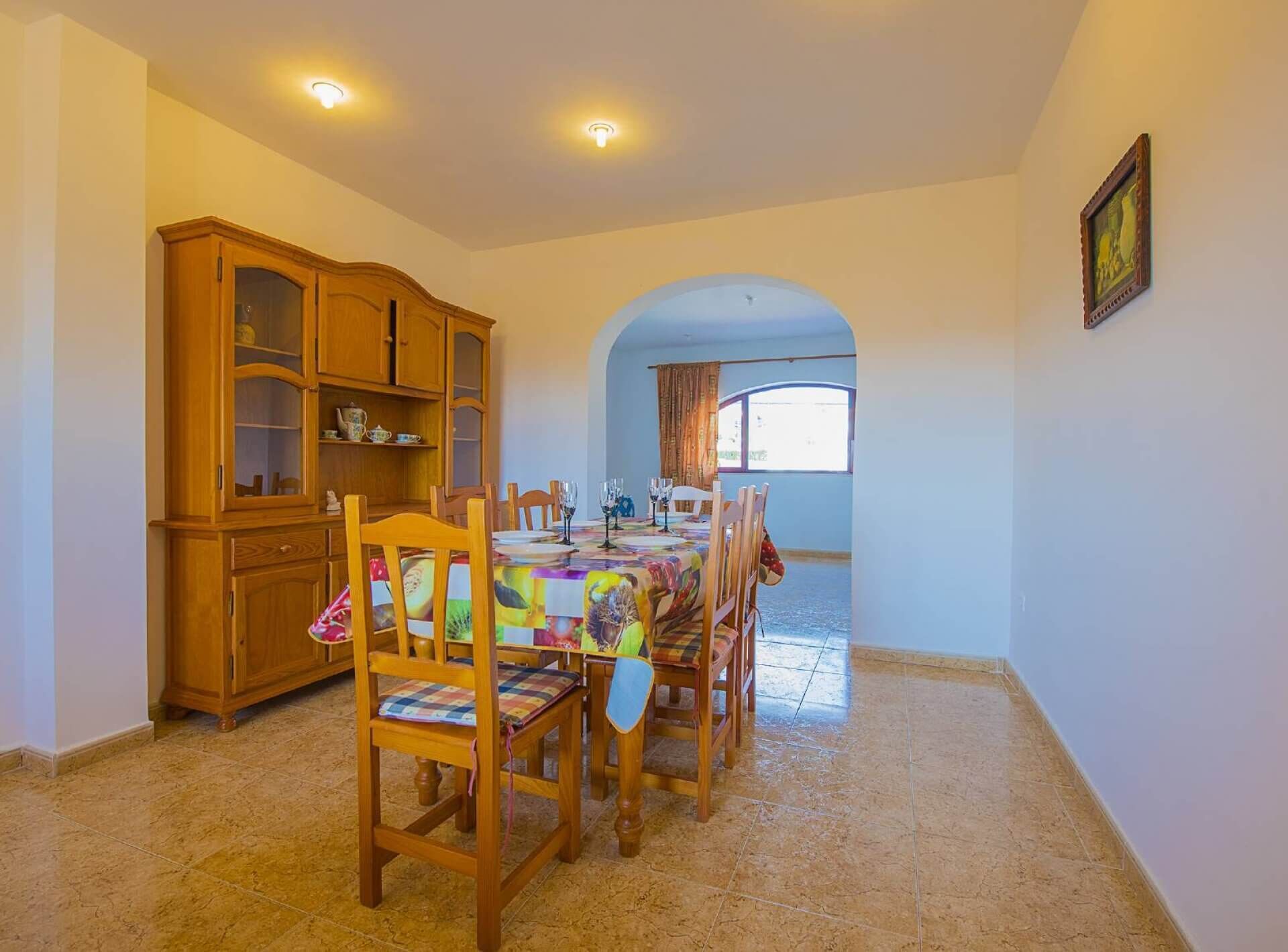 A dining area with a wooden cabinet, a table set for four, and a view through an archway to another room.