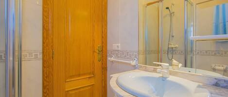 A bathroom with a wooden door, a marble sink, a glass shower enclosure, and a mirror.