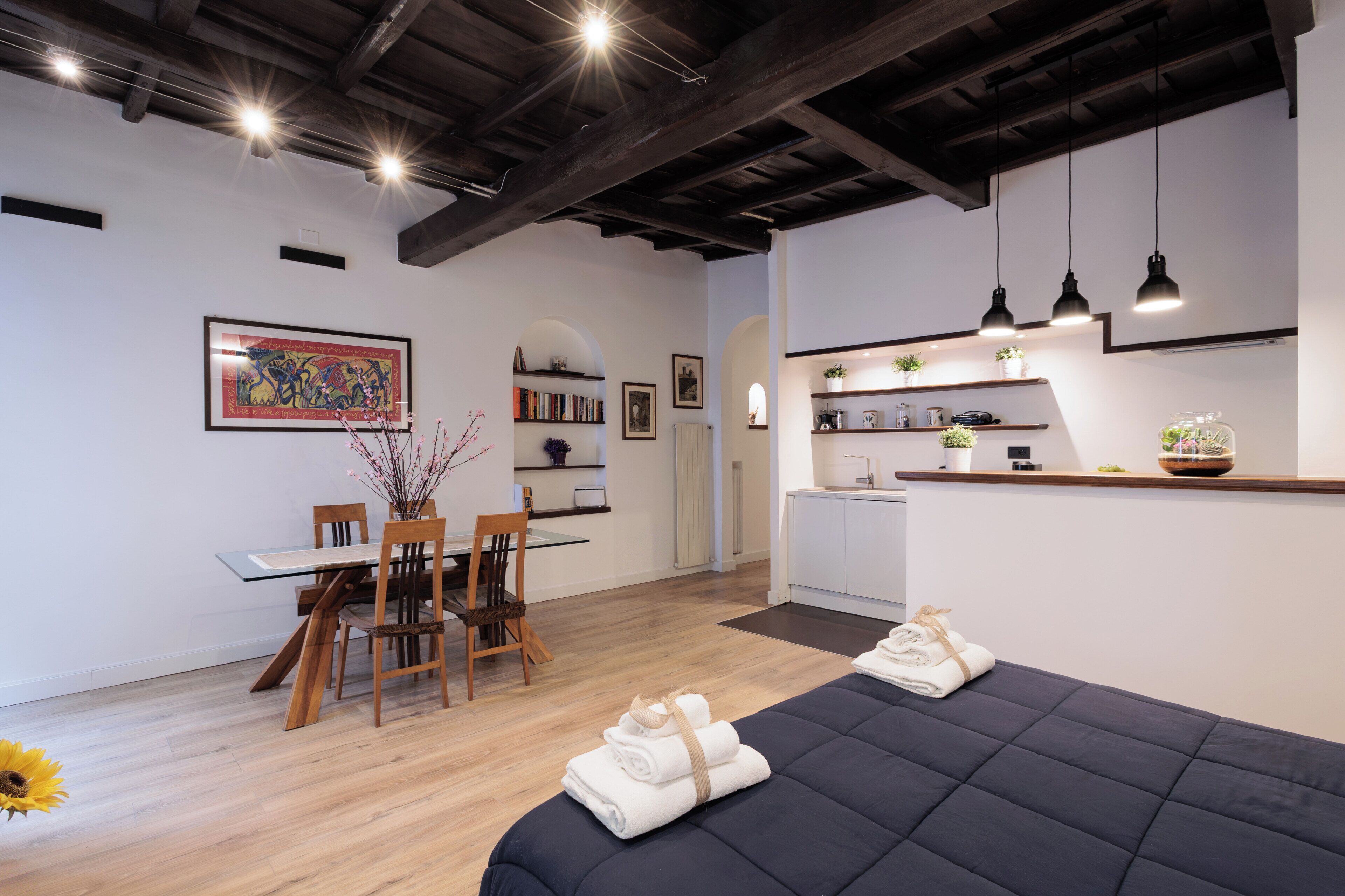 Une chambre moderne comprenant un lit, une table à manger avec des chaises, un coin cuisine et une grande œuvre d’art encadrée au mur.