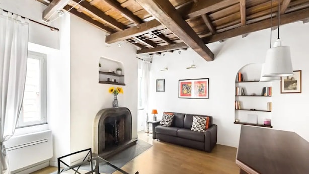A living room with exposed wooden beams, a fireplace, a sofa, and shelves with books and pictures. - Lovely Trastevere - An Authentic Experience .. (Roma)