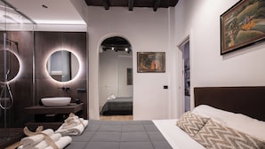 A modern bedroom with a large bed, a bedside table, a bathroom with a sink and mirror, and a hallway leading to another room. - Lovely Trastevere - An Authentic Experience .. (Roma)