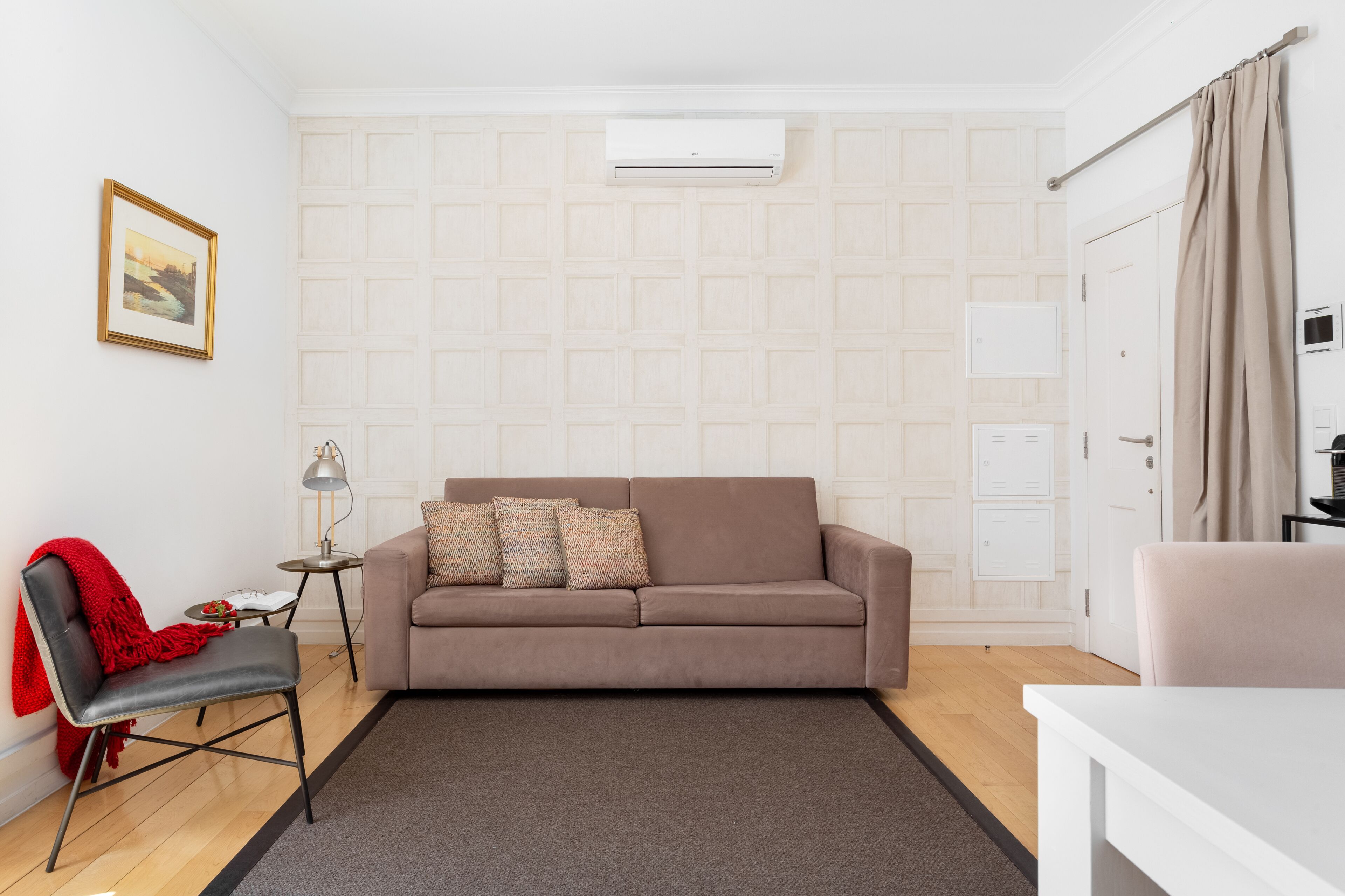 Una sala de estar moderna con un sofá color beige, una butaca roja, una mesita auxiliar y una lámpara.