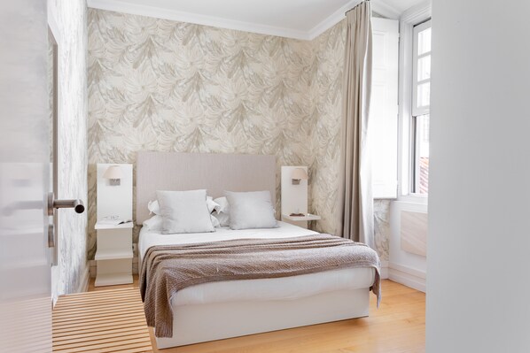 Ein Schlafzimmer mit Bett, Nachttischen, einem Fenster und einer Tür.