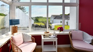 A cozy room with a large window, wicker chairs, a small table with tea set, and a view of a rural landscape.