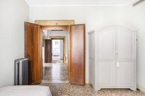 A room with a bed, a radiator, a wardrobe, and a door leading to another room.