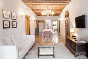 A spacious living room with a white sofa, a patterned armchair, a coffee table, and a wooden ceiling.