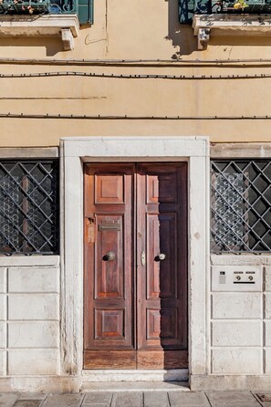 A double wooden door with a metal grid on either side, set in a beige building facade.