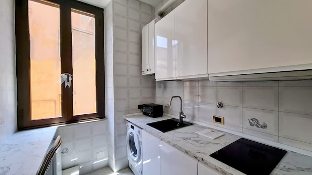 Une cuisine moderne avec des meubles blancs, un lave-linge encastré, un évier noir et un plan de travail en marbre.