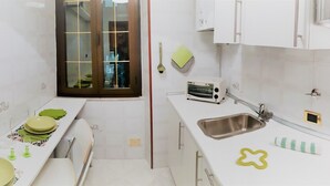 Une petite cuisine aux murs recouverts de carreaux blancs, avec un évier, un grille-pain et une fenêtre donnant sur un beau paysage.