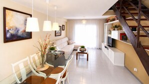 Un salon moderne comprenant un coin repas, un escalier et un téléviseur posé sur une étagère.