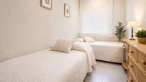 Une chambre avec deux lits, une commode, une fenêtre avec des stores et des œuvres d’art encadrées accrochées au mur.