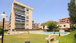 Un edificio residencial con varios balcones, piscina y una zona verde con bancos.