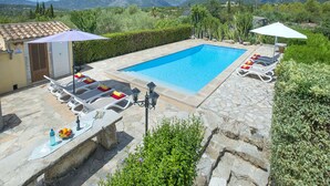 A swimming pool with lounge chairs and umbrellas, surrounded by stone tiles and greenery, with mountains in the background.