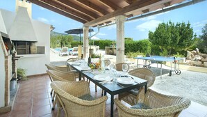 An outdoor dining area with wicker chairs and a table set for six, overlooking a pool and greenery.