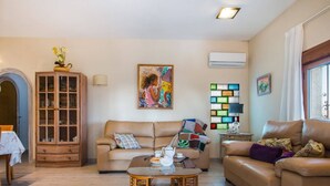 A living room with a sofa, a coffee table, a cabinet, and a wall-mounted air conditioner.