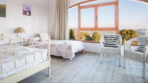 A bedroom with two beds, a window with a view, a chair, and a lamp.