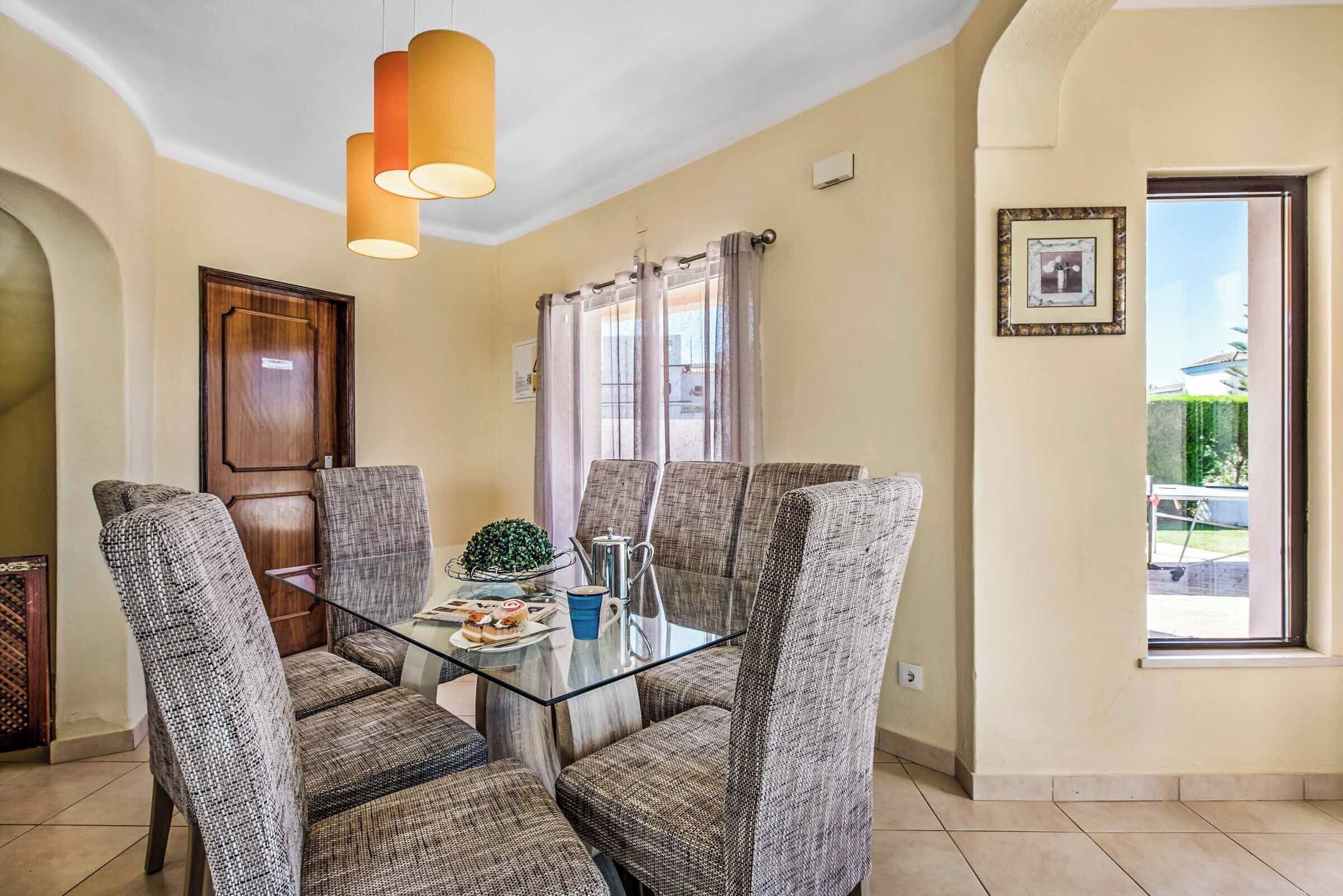 A dining area with a glass table, four upholstered chairs, a small plant, and a blue cup.
