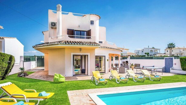 A modern two-story house with a swimming pool, yellow lounge chairs, and a well-maintained lawn.