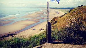 A flag on a post by a beach with a view of the ocean and distant land. - Beautiful open plan self-catering cottage surrounded by tranquil woodlands (By Arbroath)