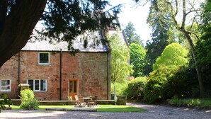 A stone building with a door and windows, surrounded by a gravel driveway and greenery. - Beautiful open plan self-catering cottage surrounded by tranquil woodlands (By Arbroath)