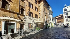 Une rue pavée bordée d’immeubles, un magasin fermé avec une enseigne, et une clôture en métal.