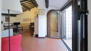Un salon comprenant un canapé, une table basse, un téléviseur et une lampe. On y trouve également une cheminée, une table à manger avec des chaises, et un escalier menant à un balcon.