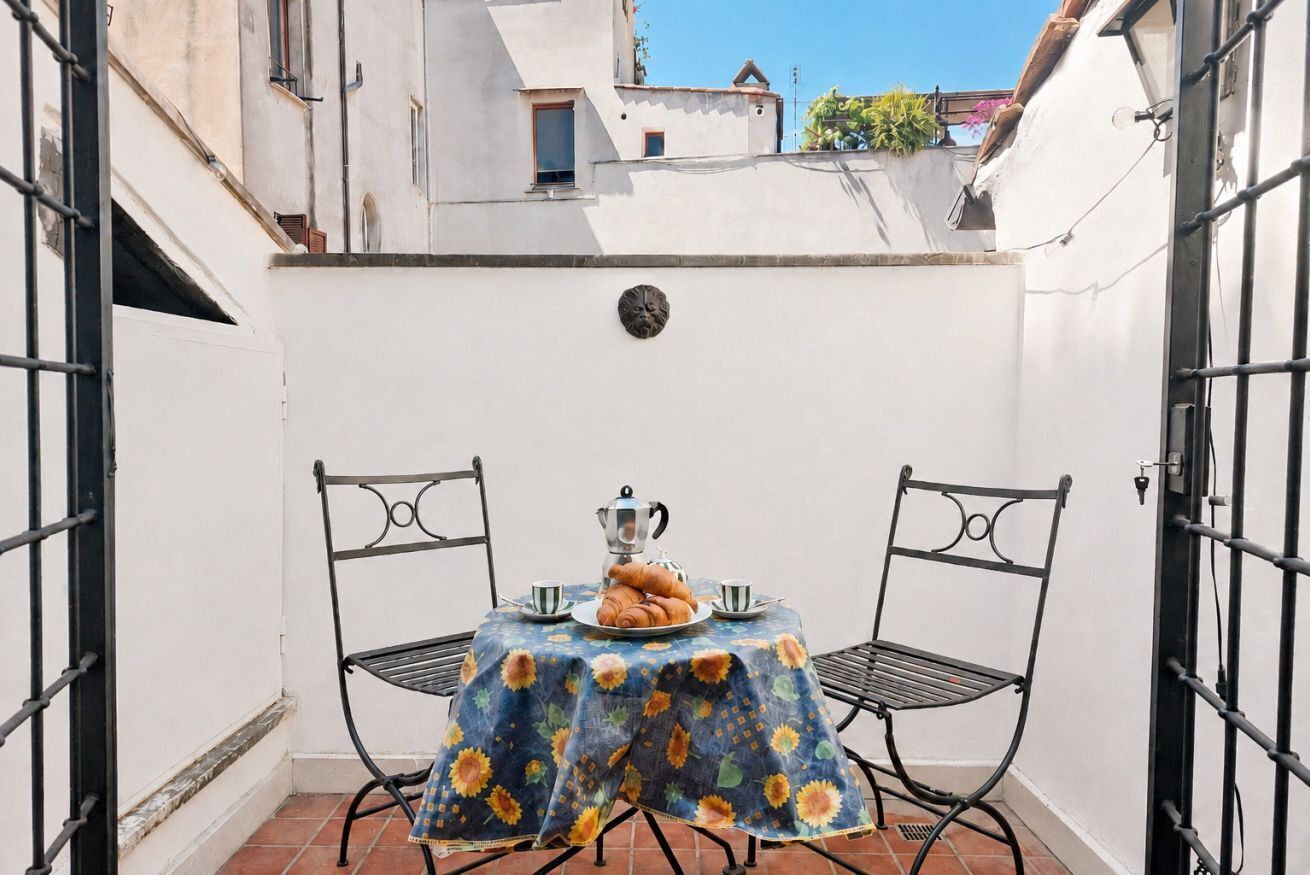 A small outdoor patio with a table set for breakfast, two chairs, and a decorative wall plate.