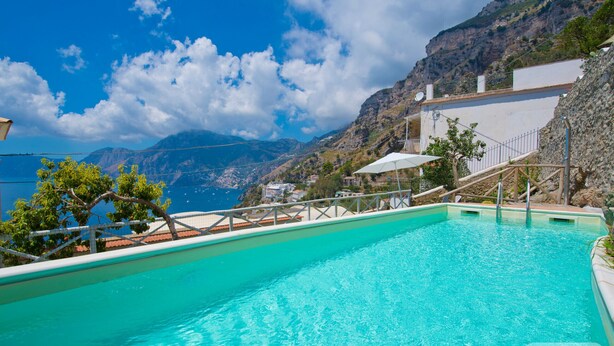 Une piscine à l’eau cristalline, entourée d’un paysage montagneux et d’un bâtiment doté d’un balcon donnant sur la piscine.