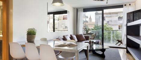 A modern living room with a dining area, large windows, and a view of the cityscape.