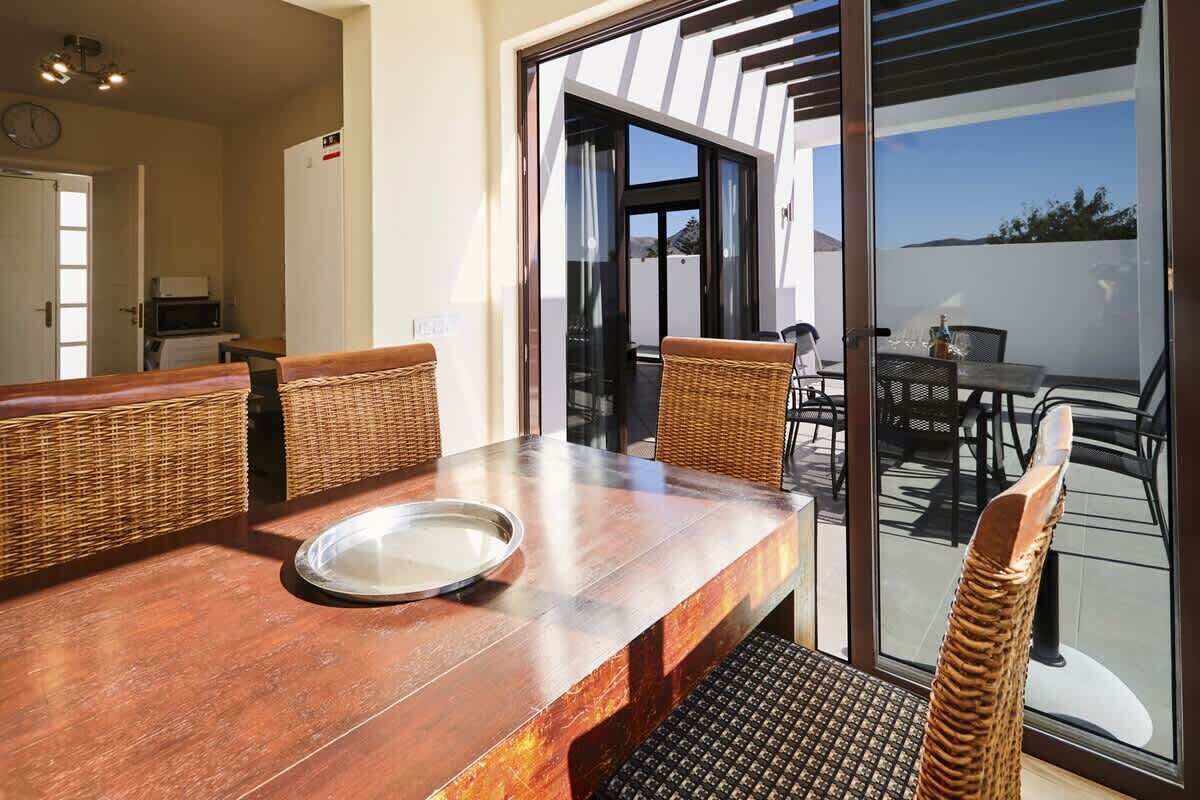 A dining area with a wooden table, wicker chairs, and a glass door leading to an outdoor patio.