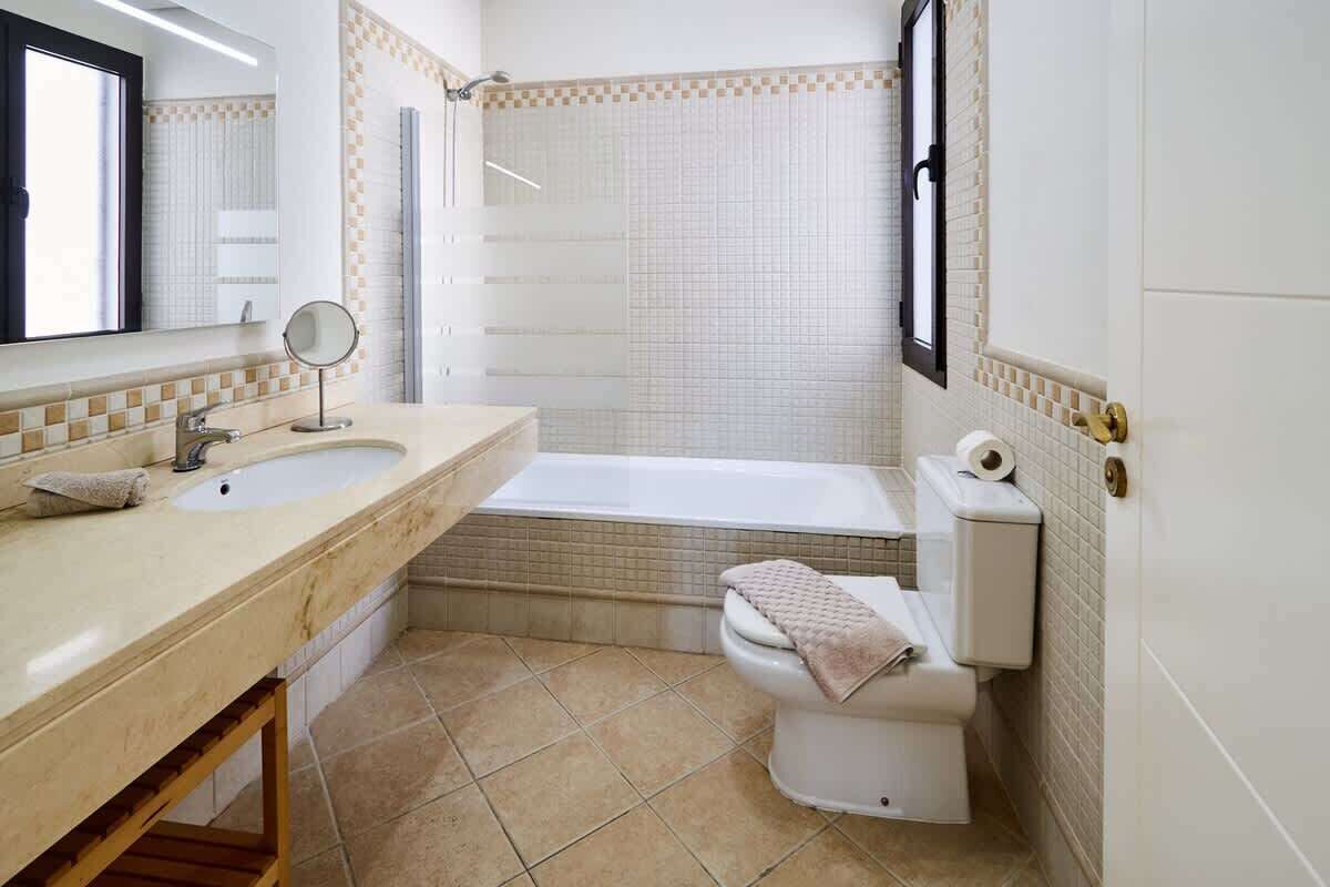 A bathroom with a sink, mirror, bathtub, toilet, and a towel on the toilet.