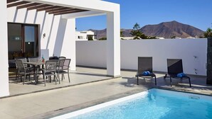 A modern outdoor pool area with a pergola, seating, and a mountain view.